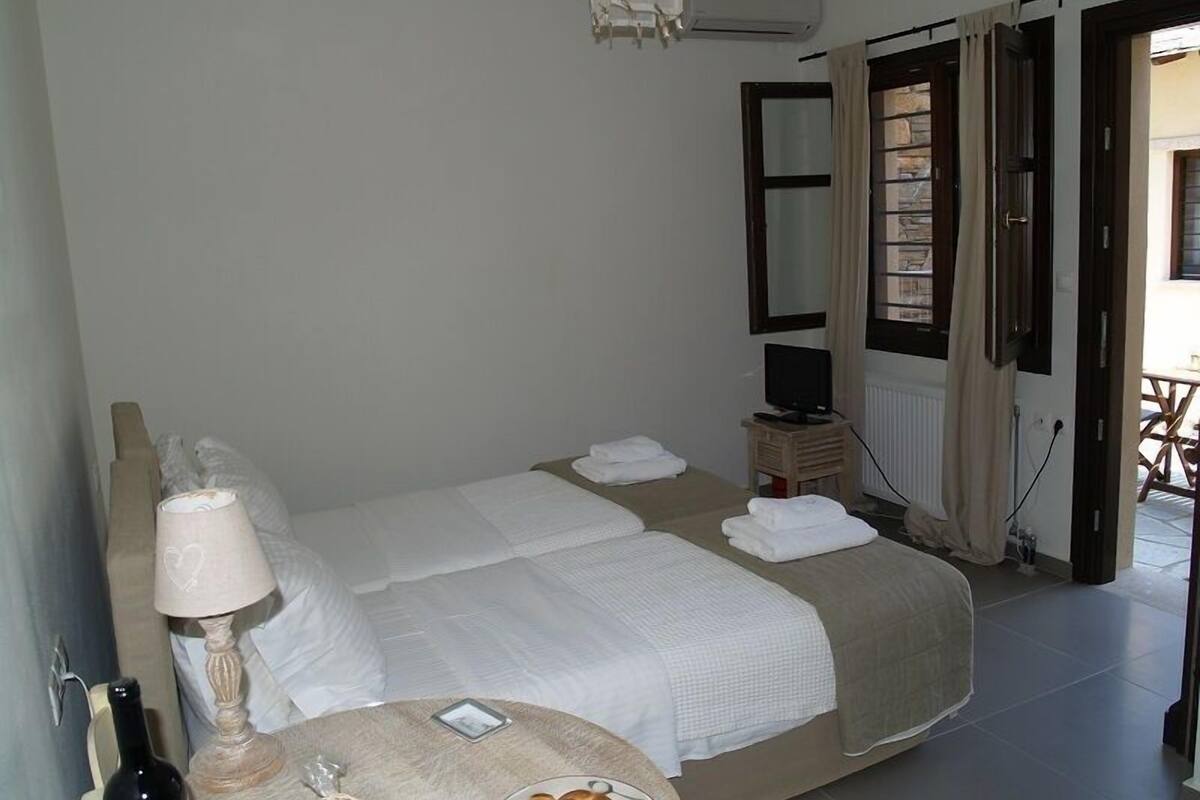 Un dormitorio con cama, mesita de noche con lámpara, televisor y ventana con cortinas.