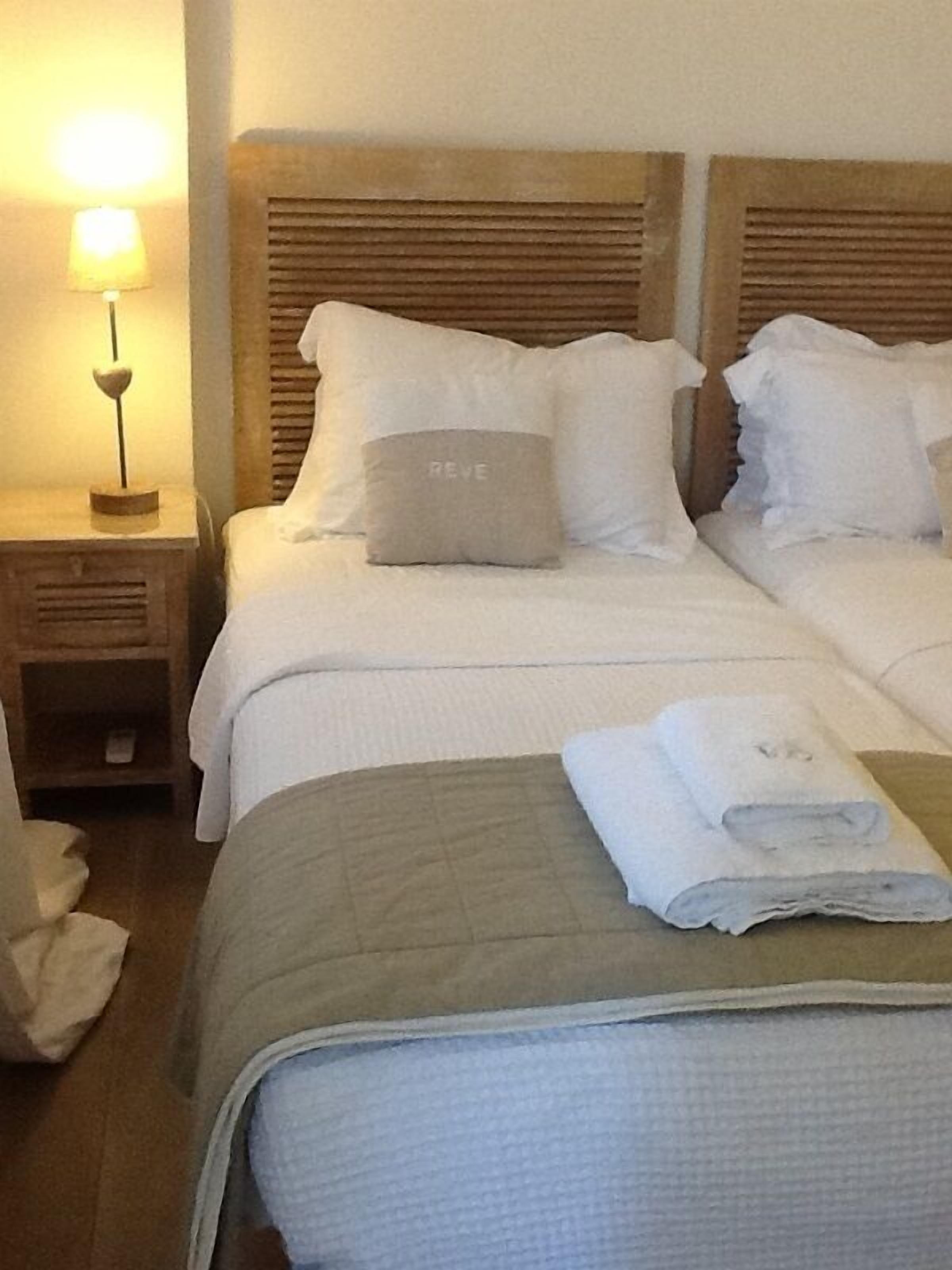 A hotel room with two beds, a nightstand with a lamp, and a folded towel on the bed.