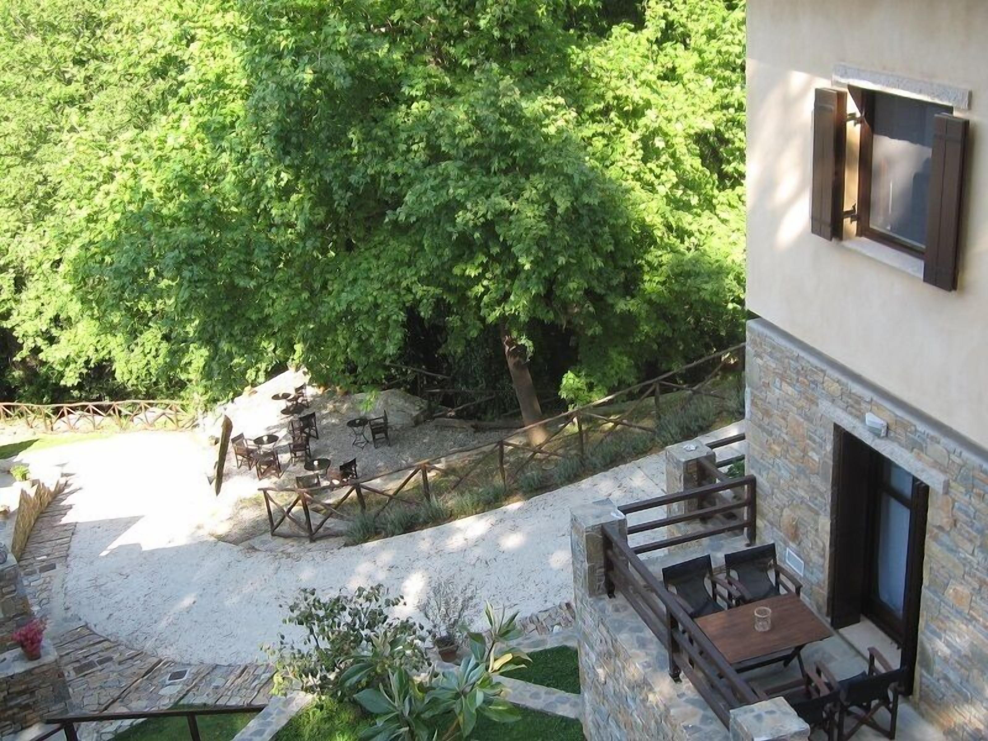 A stone building with a fireplace, outdoor seating area, and a view of dense green trees.