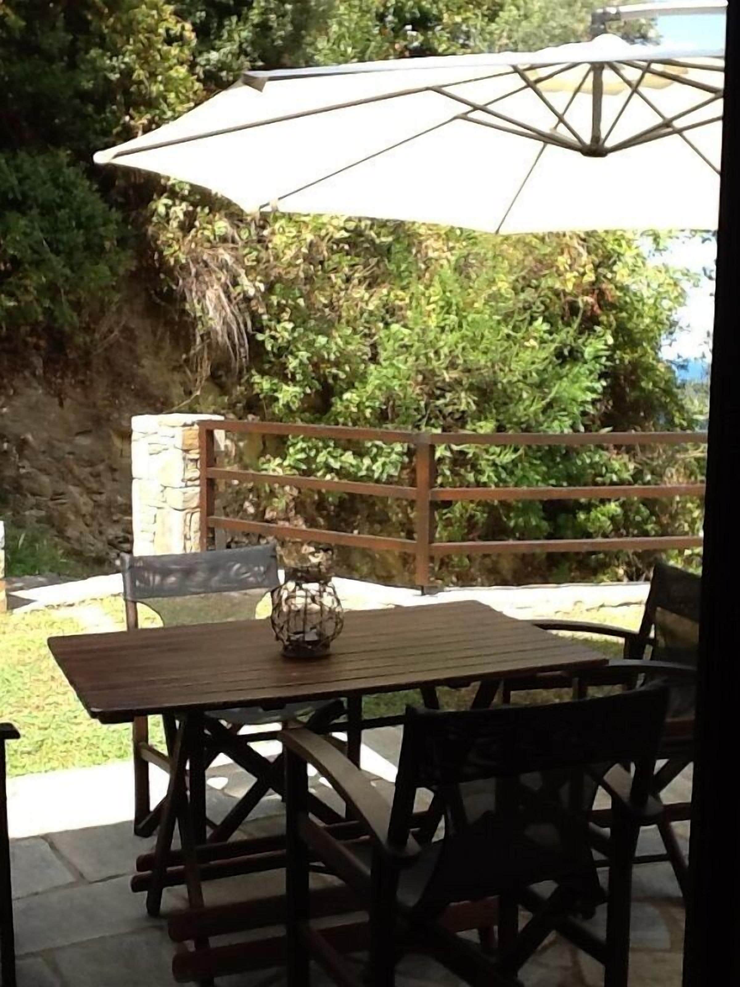 An outdoor patio with a wooden table and chairs, a metal lantern, and a white umbrella.