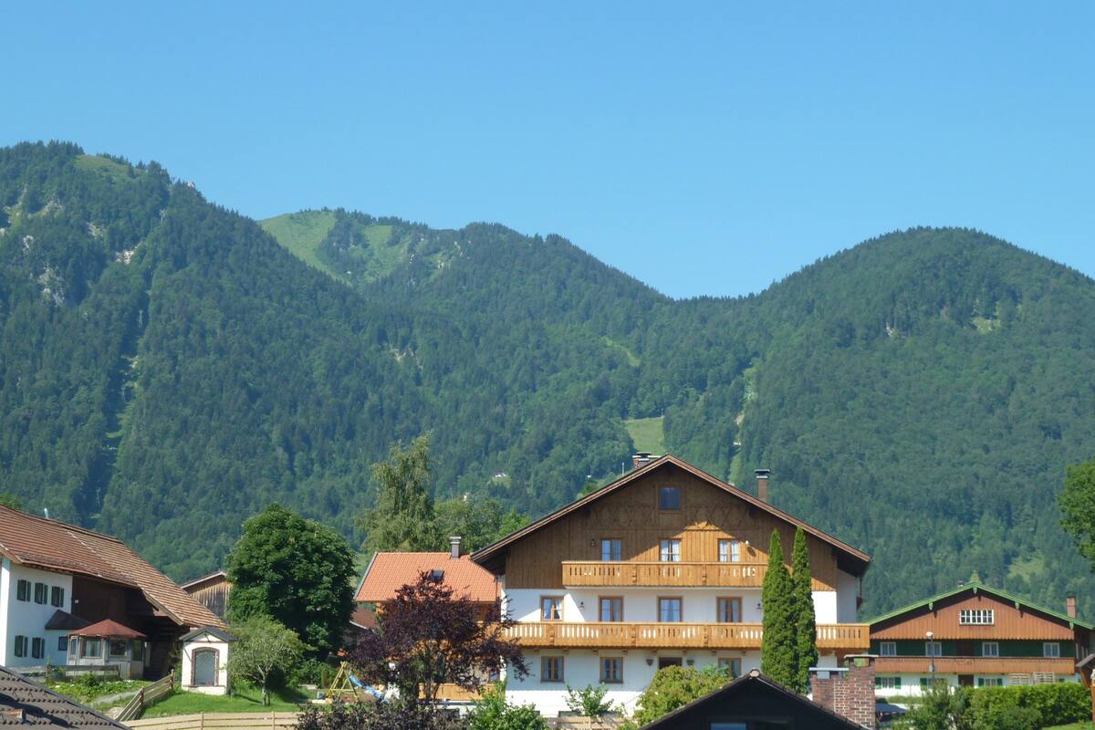 A traditional chalet-style building with a wooden facade, multiple balconies, and a view of a forested mountain range.