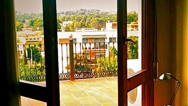 A room with a large sliding glass door leading to an outdoor balcony with a view of buildings and greenery. - Hostal del Carmen (Terrassa)