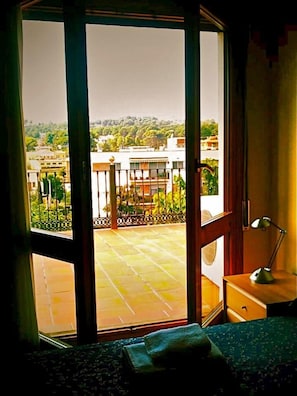 A room with a large sliding glass door leading to an outdoor balcony with a view of buildings and greenery. - Hostal del Carmen (Terrassa)