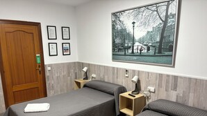 A hotel room with two beds, a wooden door, a framed certificate on the wall, and a cityscape painting. - Hostal del Carmen (Terrassa)
