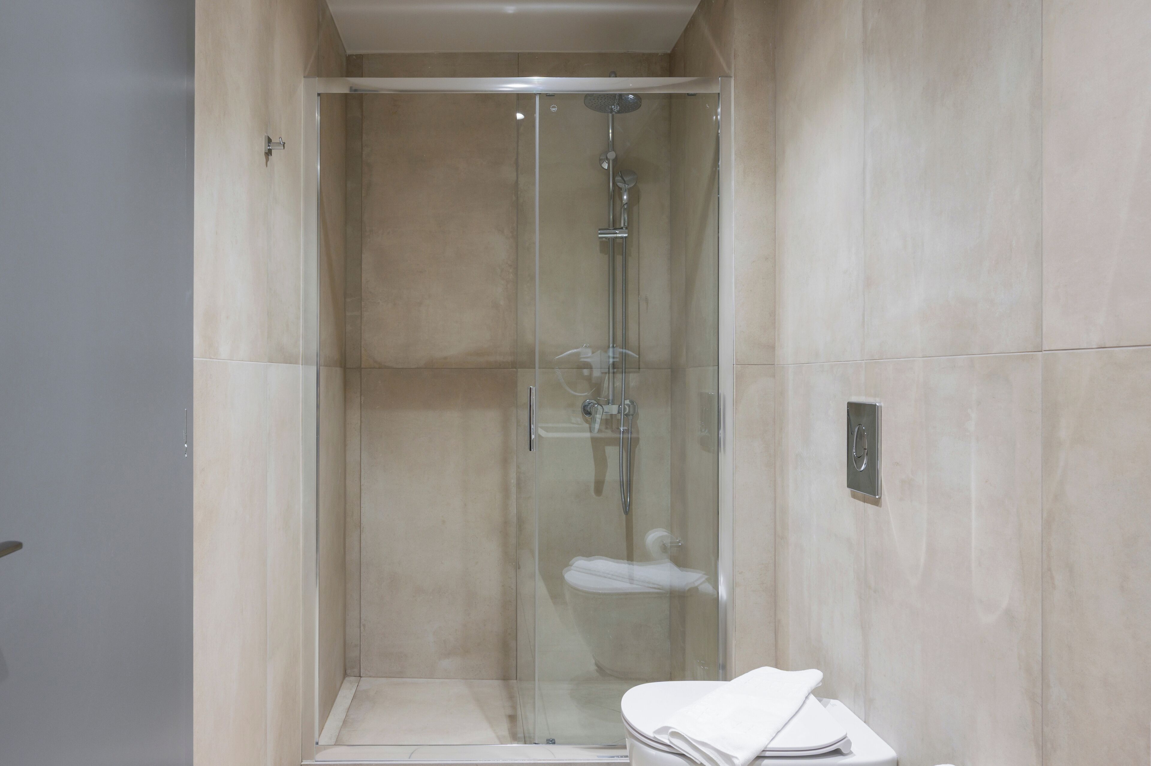 A glass-enclosed shower with a handheld showerhead and a wall-mounted faucet.