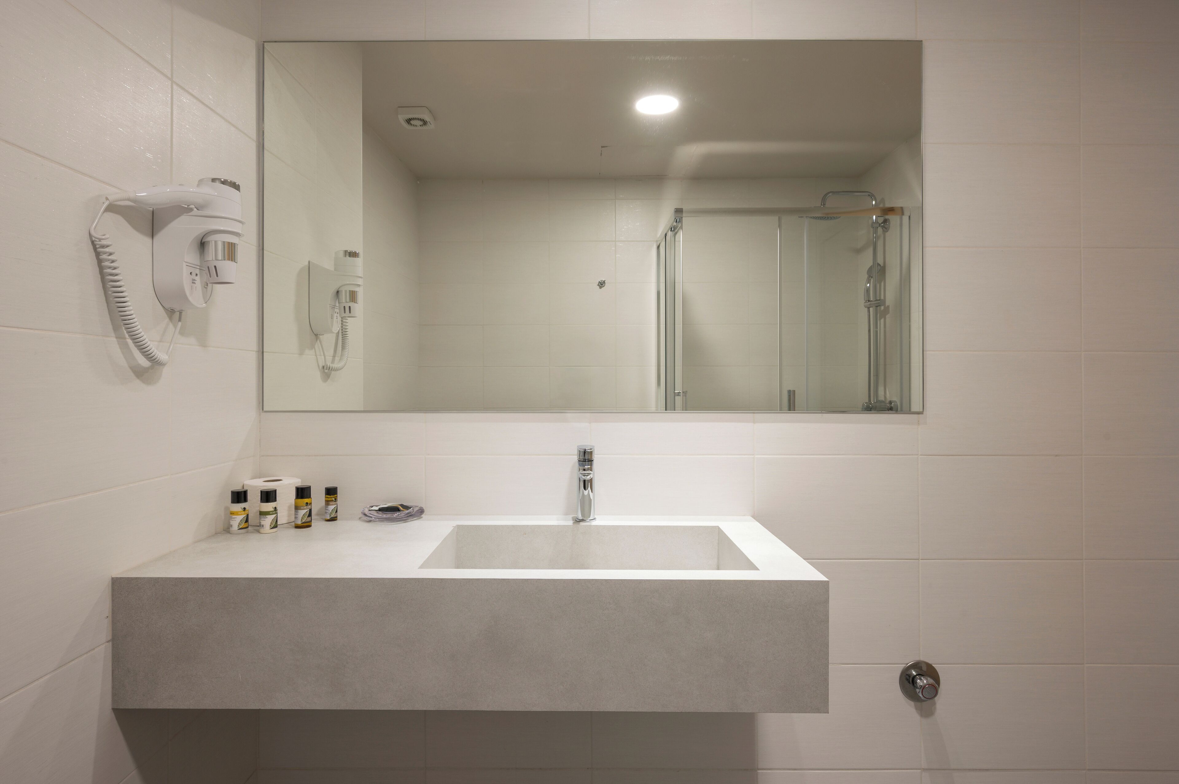 A bathroom with a large mirror, a sink, a hairdryer, and a shower.
