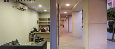 A reception area with a reception desk, chairs, and a computer. There is a hallway leading to other parts of the building.