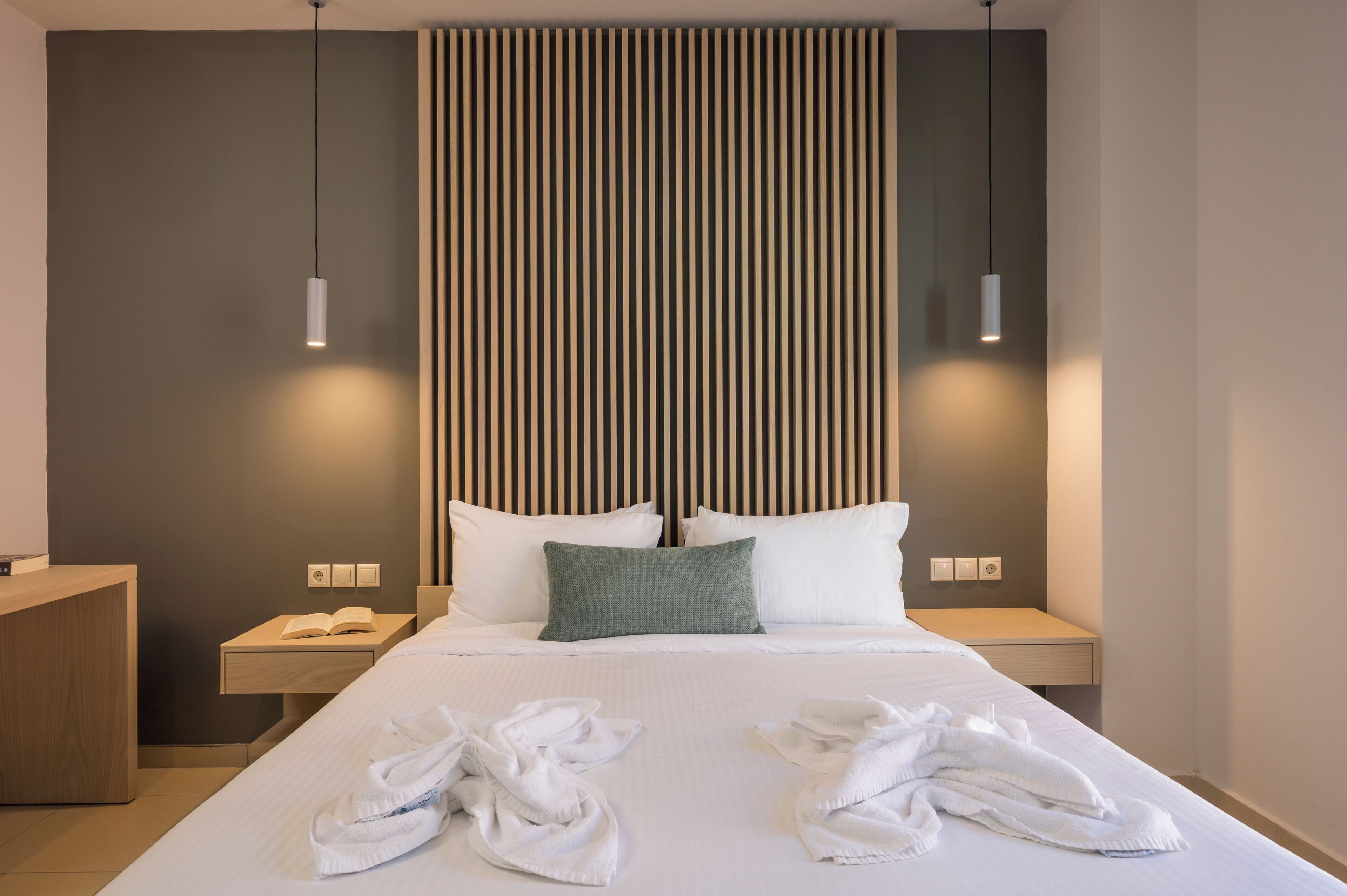 Una habitación de hotel moderna con una cama grande, dos mesitas de noche, un cabecero de madera y un panel de luz integrado en la pared.