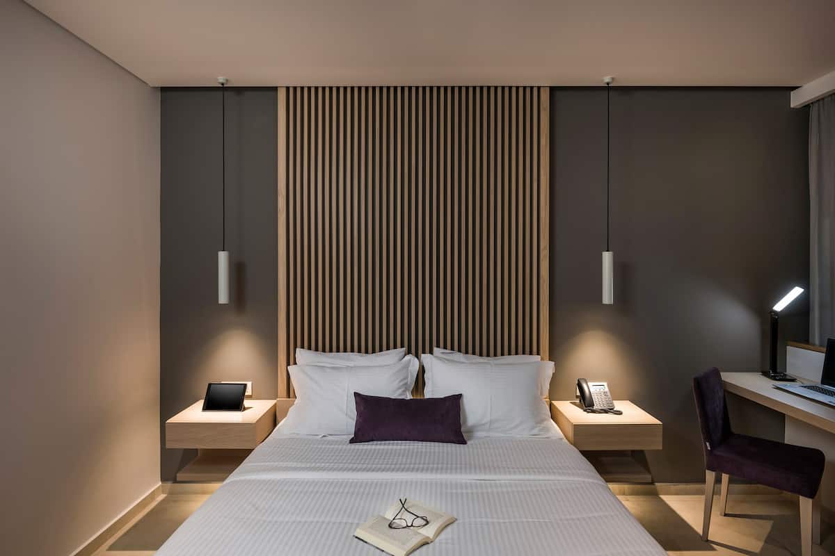 Una habitación de hotel moderna con una cama grande, mesitas de noche, un escritorio y una computadora.