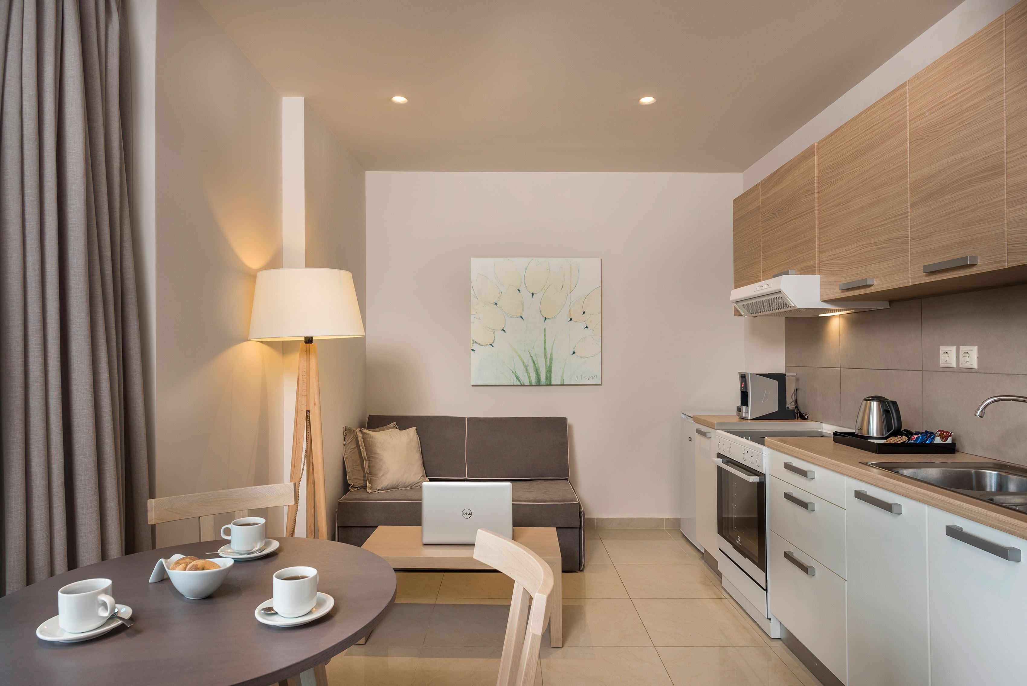 A modern kitchen with a dining area, including a table with cups and a bowl, a sofa, and a lamp.