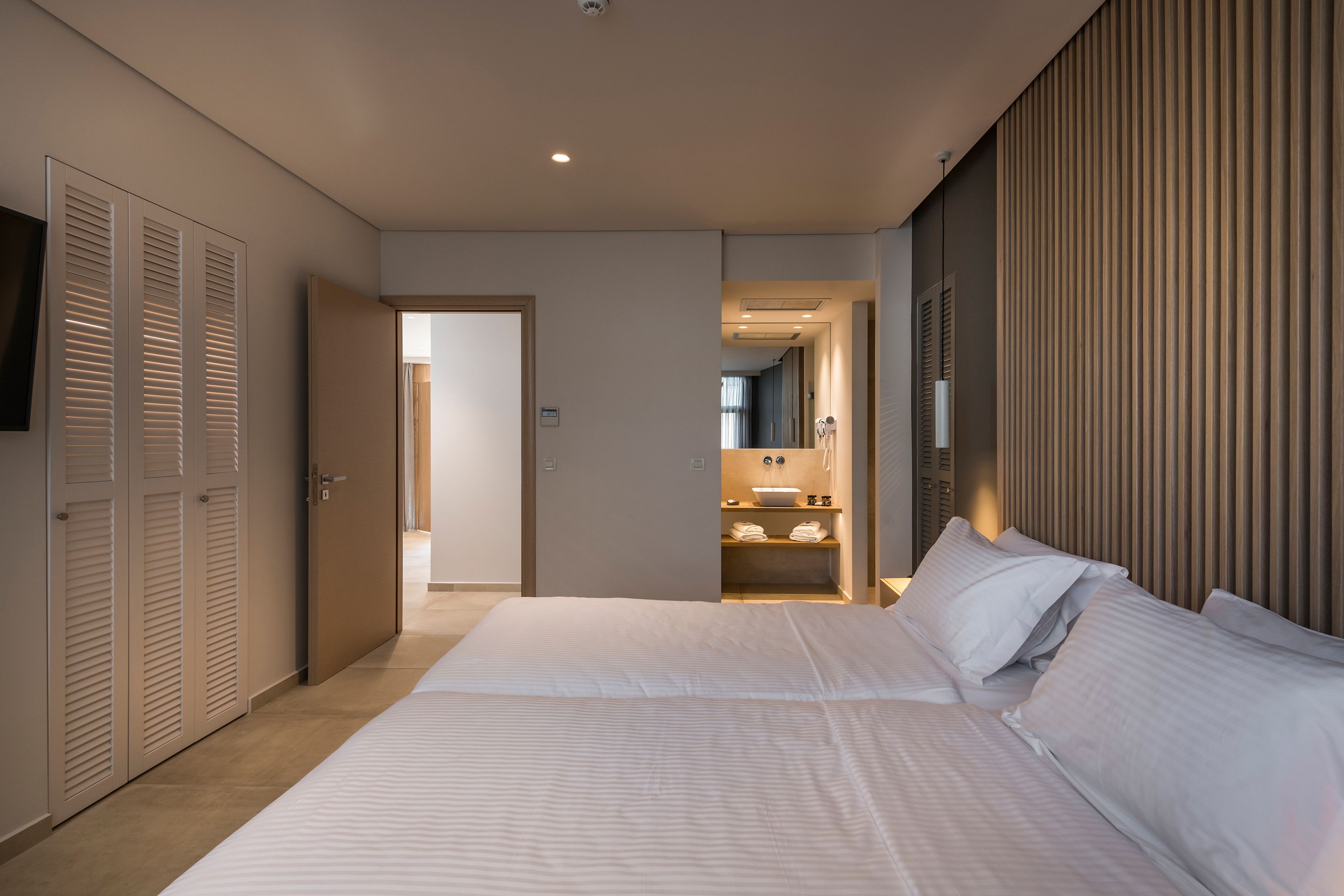 A modern hotel room with a large bed, a walk-in closet, and a bathroom with a vanity and mirror.