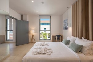 Et moderne hotelværelse med en stor seng, et skrivebord, en stol og et vindue med udsigt til bygninger, samt en dør.