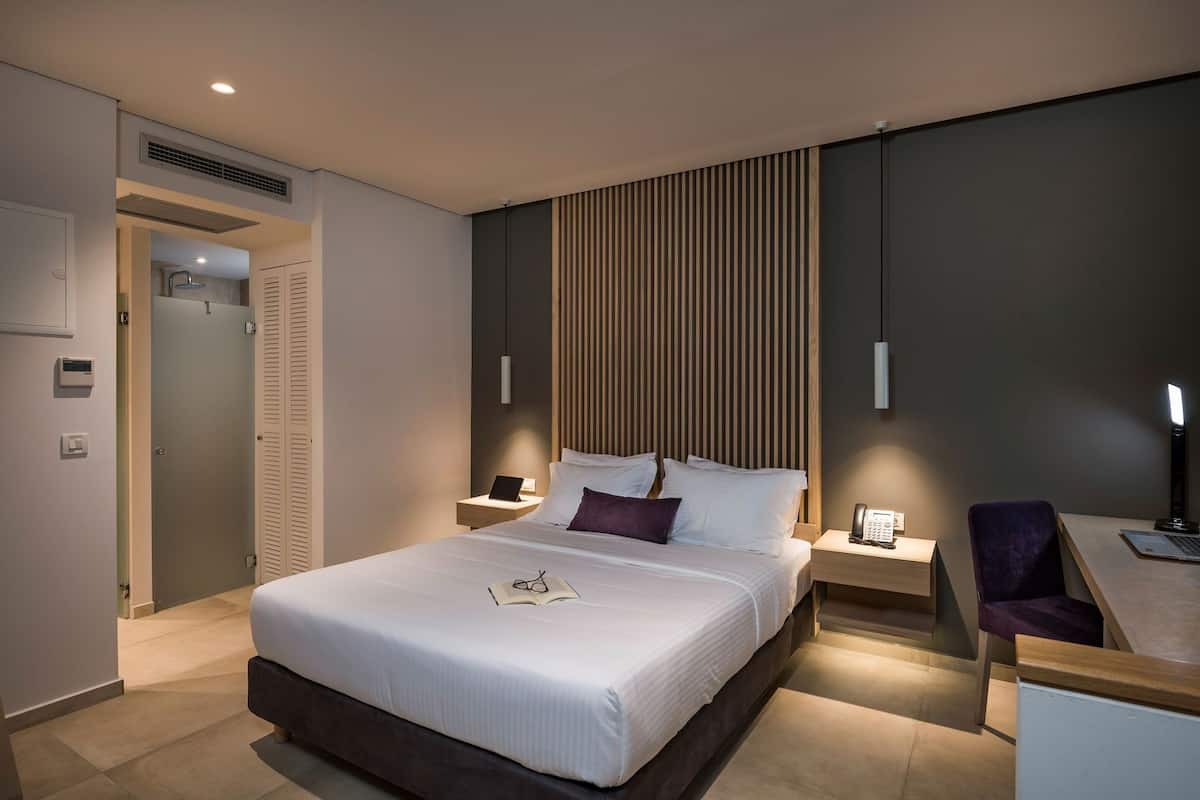 Una habitación de hotel moderna con una cama grande, mesitas de noche, un escritorio con silla y un armario.