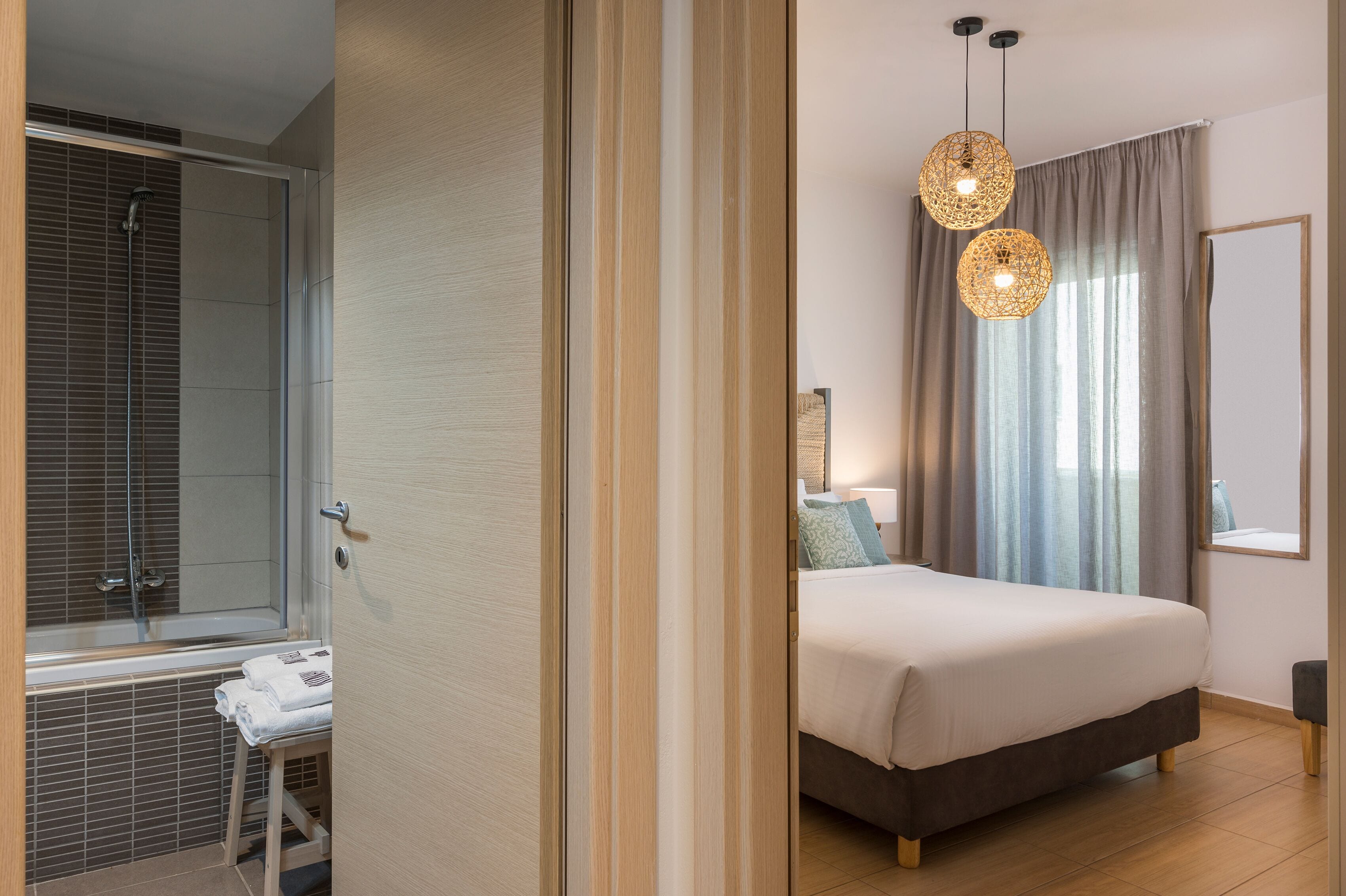 A modern bedroom with a large bed, a bedside table, a mirror, and a window with curtains.