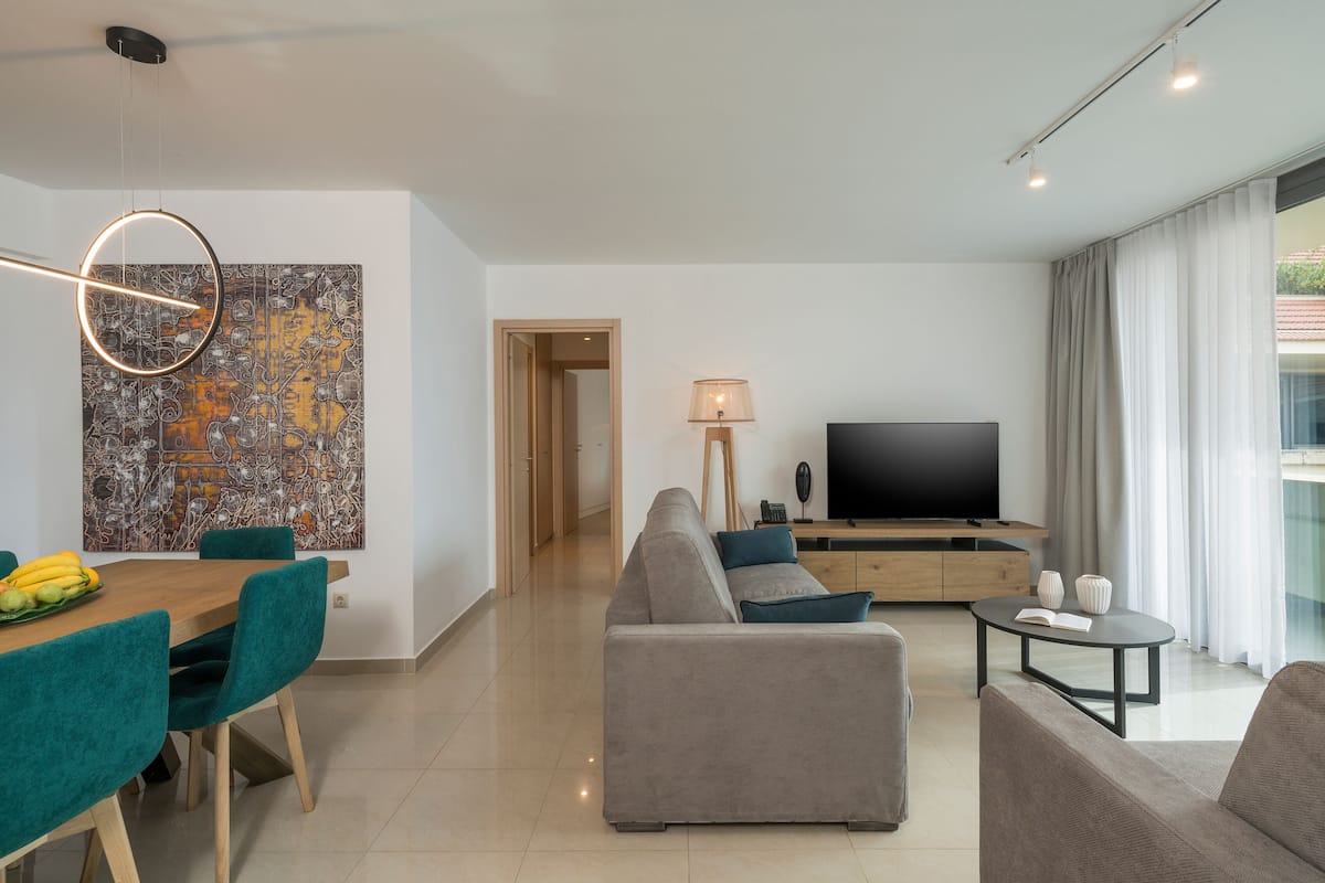 Una sala de estar moderna con un sofá, una mesa de comedor con sillas, un televisor y obras de arte en la pared.