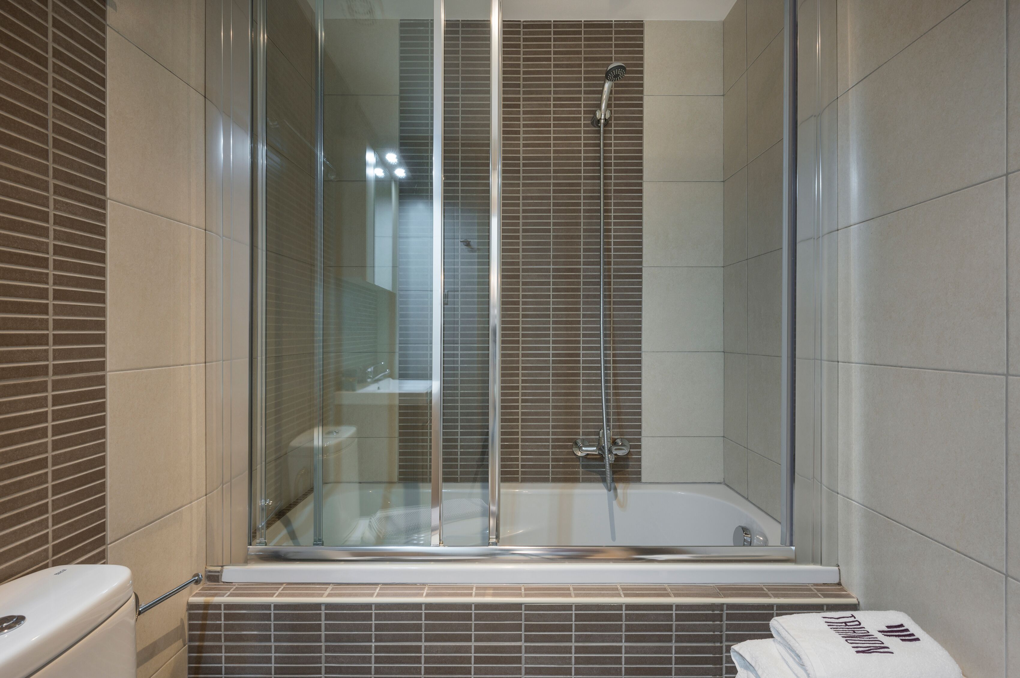 A modern bathroom with a glass-enclosed shower, a bathtub, and tiled walls.