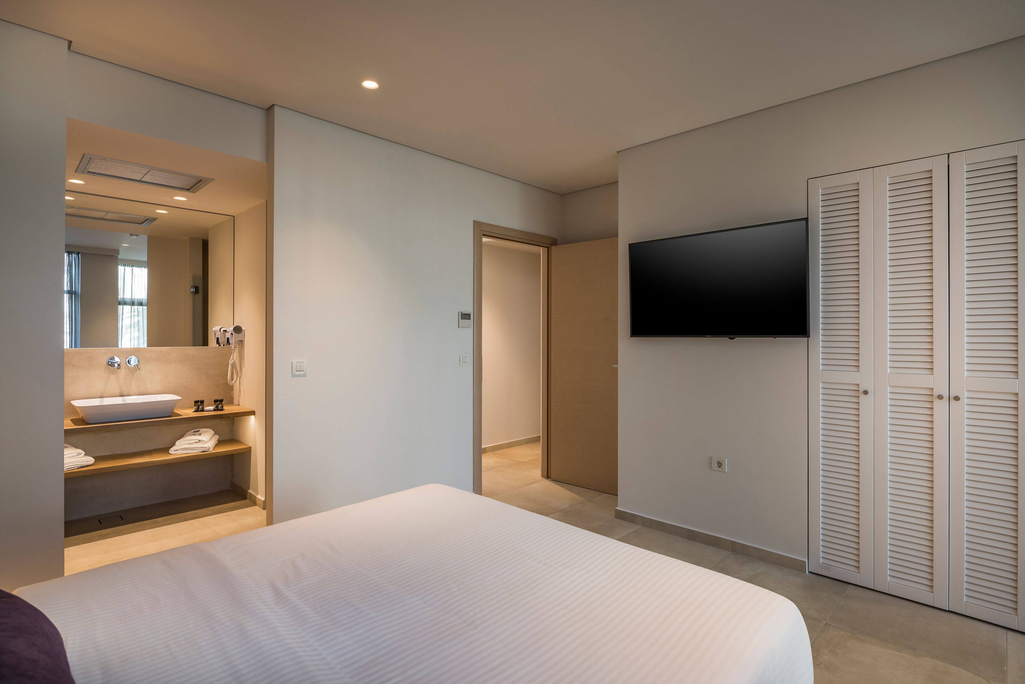 Una habitación de hotel moderna con una cama grande, un lavamanos integrado, un espejo, un televisor y un vestidor.