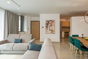 A modern living room with a sofa, a dining table with chairs, a kitchen area, and a door.
