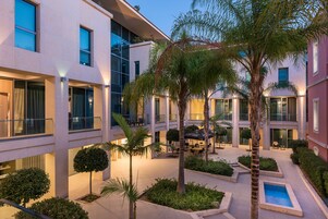 Cortile moderno di un hotel con diversi piani, sedute all'aperto e palme.