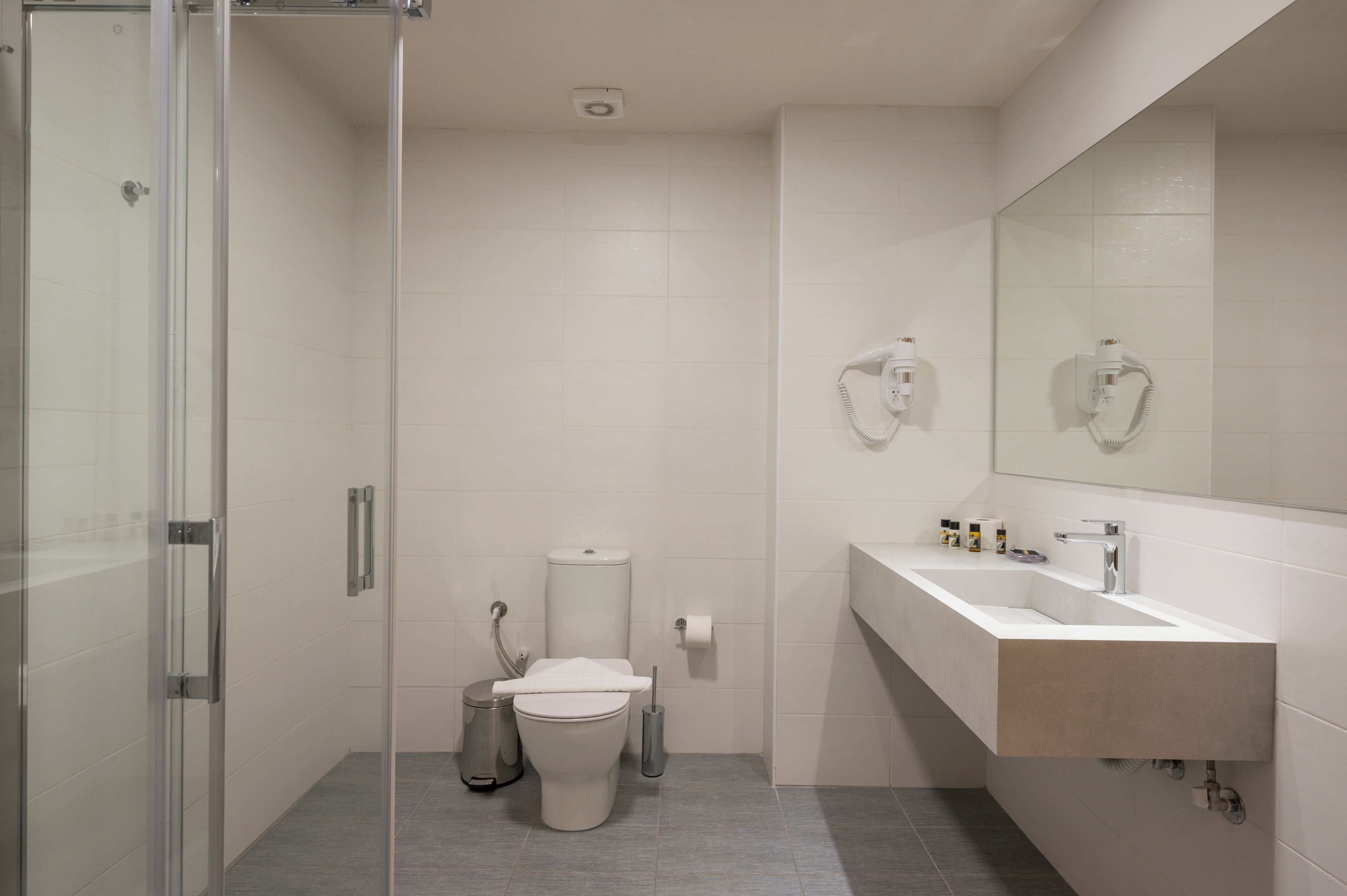A modern bathroom with a glass shower enclosure, a white sink with a beige countertop, and a large mirror above the sink.