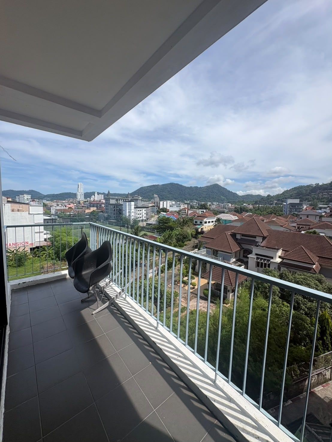 A balcony with a view of a cityscape, including buildings and mountains.