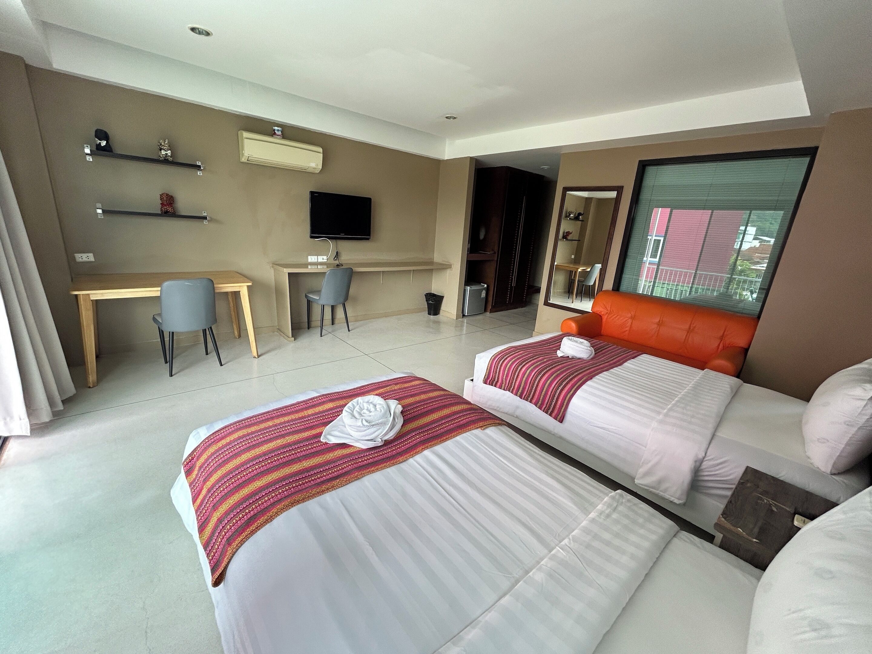 Een hotelkamer met twee bedden, een bureau, een stoel, een televisie en een groot raam.