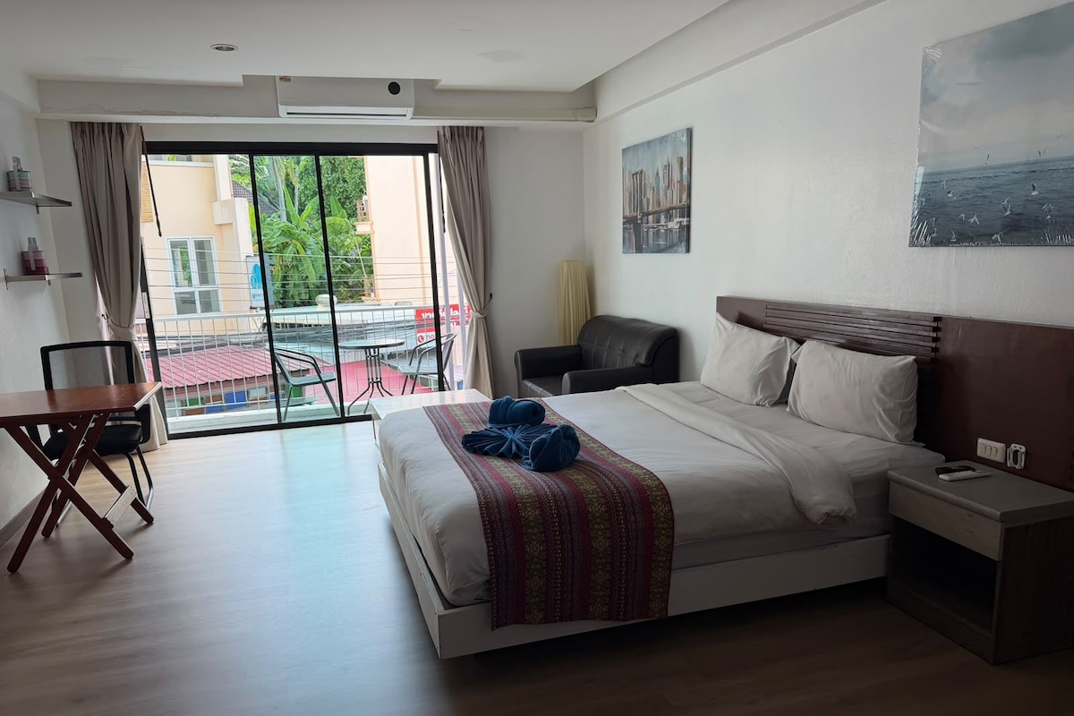 Habitación de hotel con cama, escritorio, silla, mesita de noche y vistas al exterior.