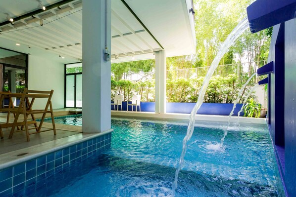 Una piscina interior con agua cristalina, una silla de madera y una zona cubierta con vistas a zonas verdes.