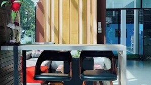 A modern interior with a wooden partition, two black chairs with cushions, and a glass door leading to a blue room. - Coco Boutique Hotel (Patong)