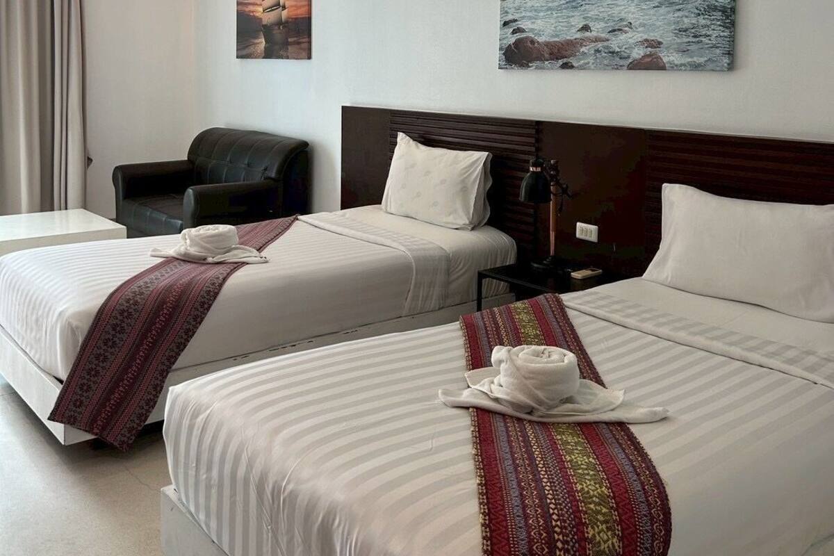 A hotel room with two beds, a chair, and two paintings on the wall.