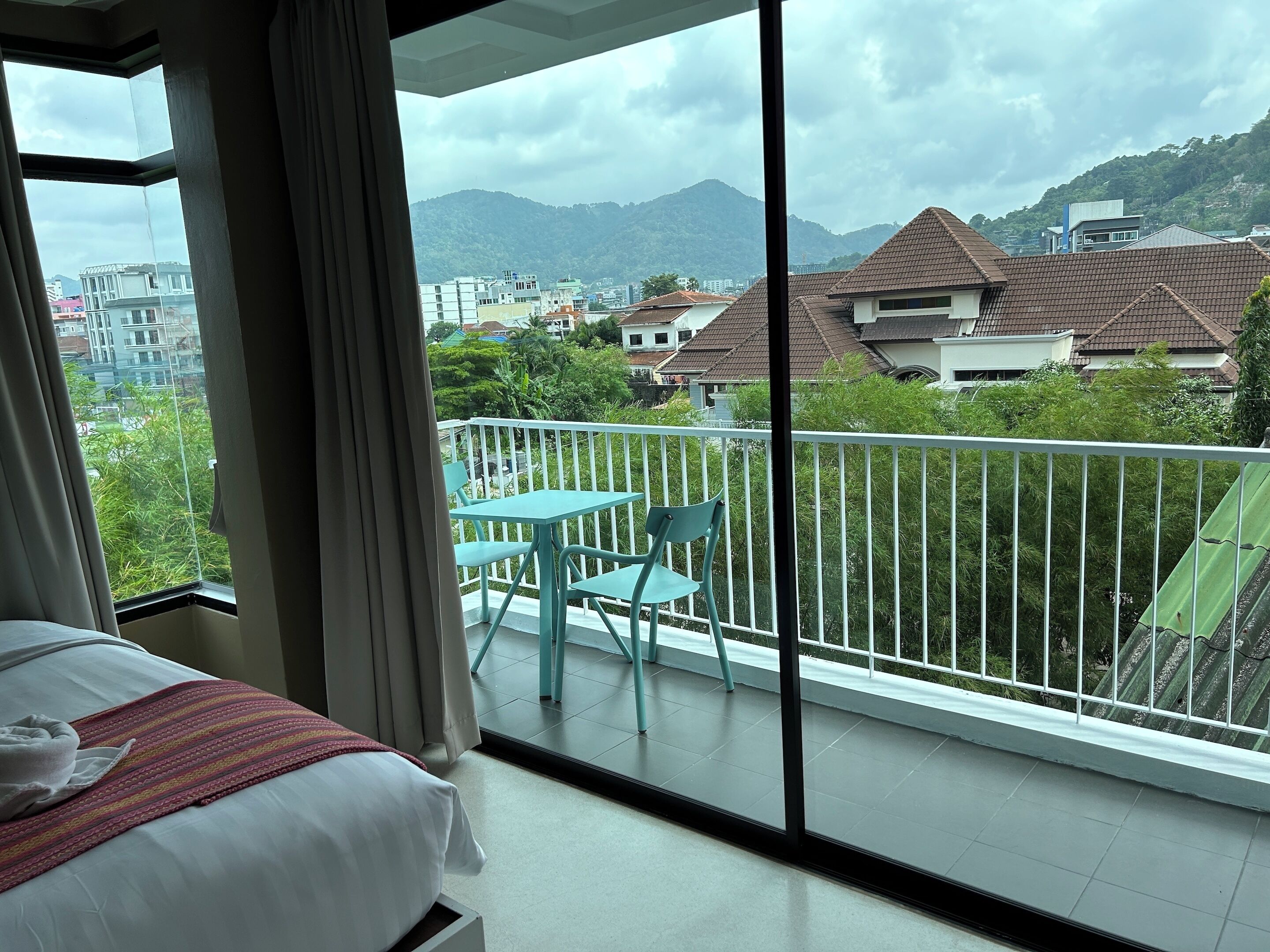 Hotelkamer met balkon, bed met een gestreept deken en uitzicht op de stad en bergen.