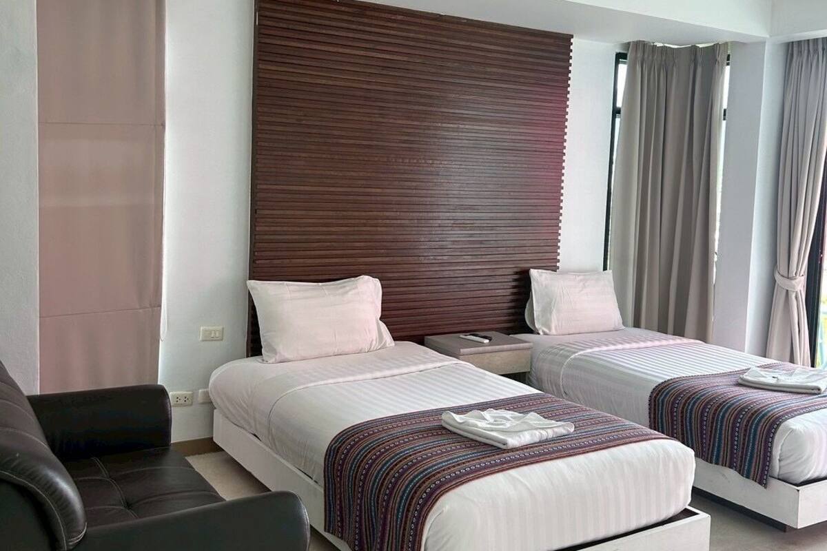 A modern hotel room with two beds, a sofa, and a large window with curtains.