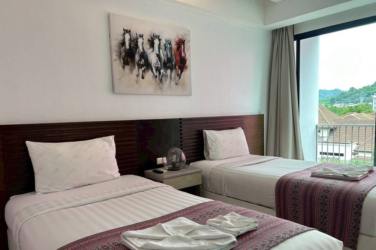 A hotel room with two beds, a painting of horses on the wall, a view of a cityscape through the window, and a balcony with a railing.