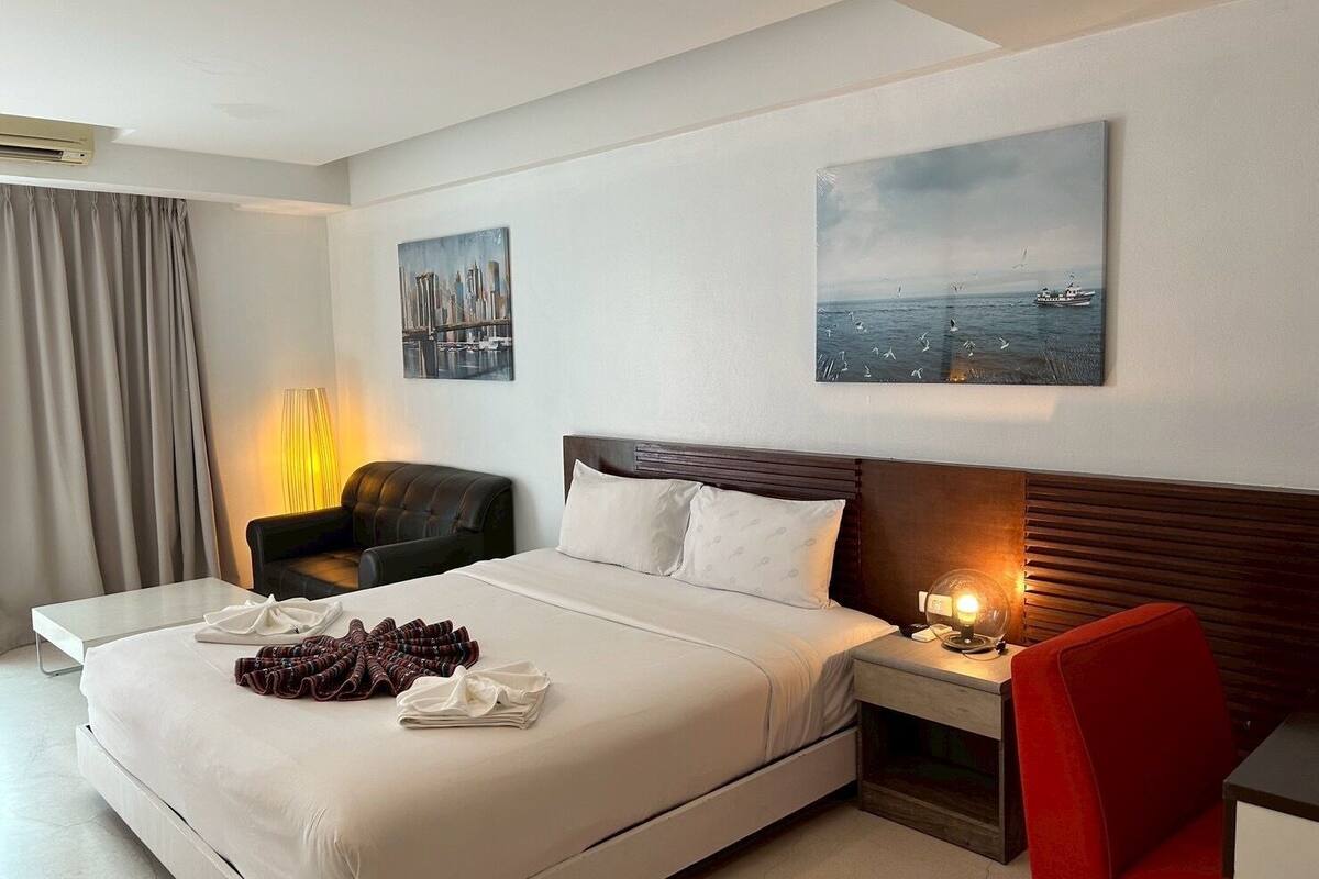 A modern hotel room with a large bed, a chair, a desk, and artwork on the walls.