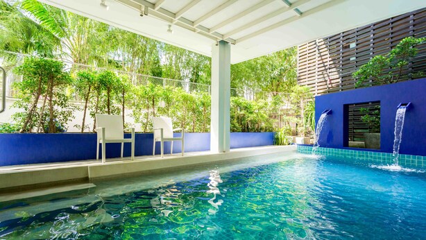 A clear indoor swimming pool with a blue-tiled edge, a white chair, and a waterfall feature. - Coco Boutique Hotel (Patong)