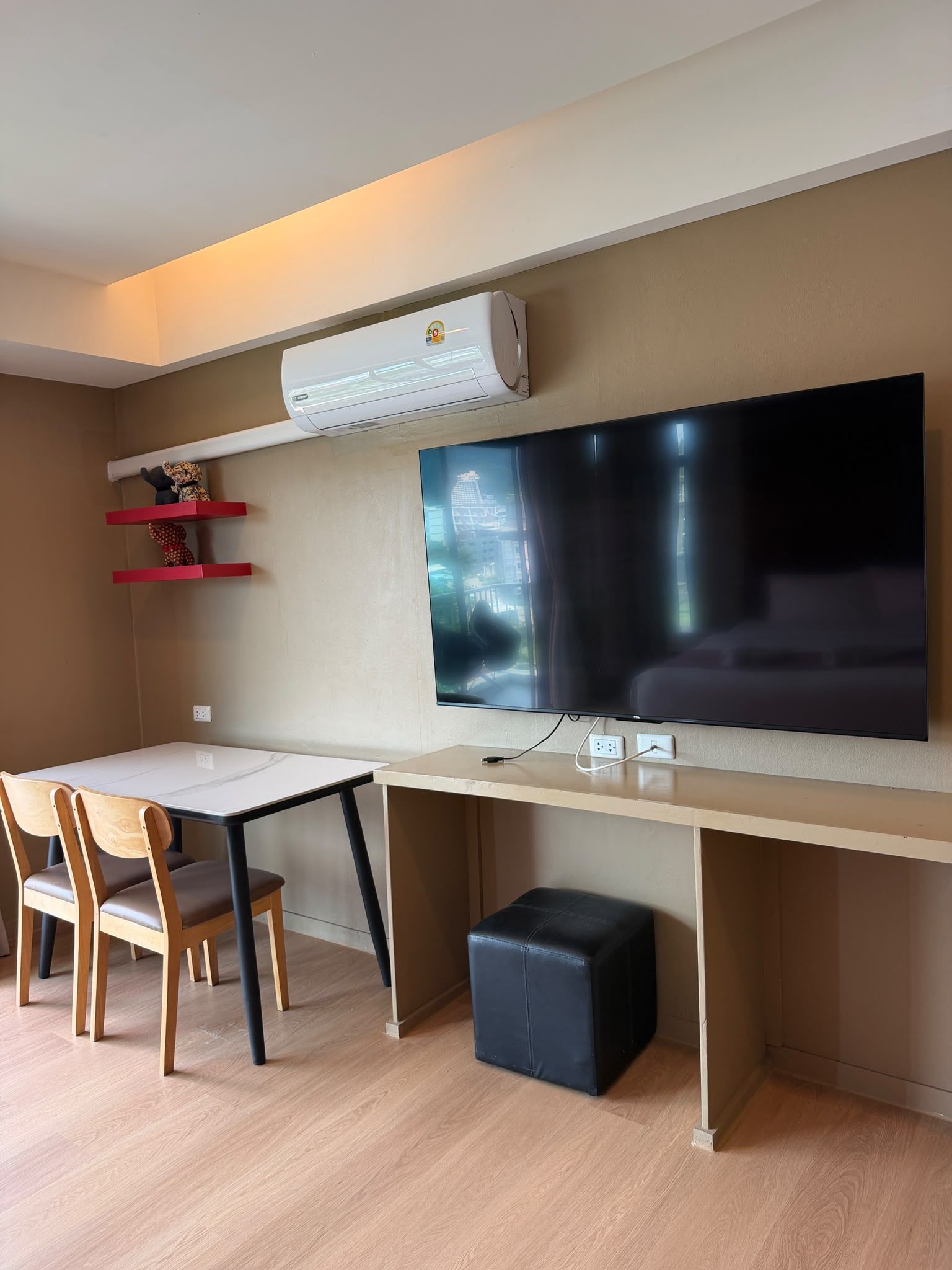 Une chambre moderne dotée d’un téléviseur à écran plat fixé au mur, d’un bureau avec des chaises et d’un petit pouf noir.