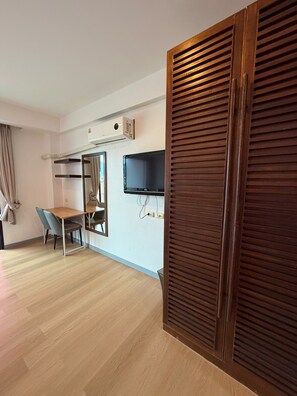 A hotel room with a wooden floor, a desk with a chair, a television mounted on the wall, and a sliding wooden door. - Coco Boutique Hotel (Patong)