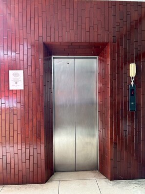Un ascensor metálico con un cartel en la pared y un teléfono a la derecha.