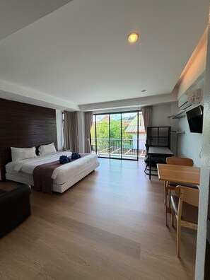A modern hotel room with a large bed, a desk, and a balcony with a view. - Coco Boutique Hotel (Patong)