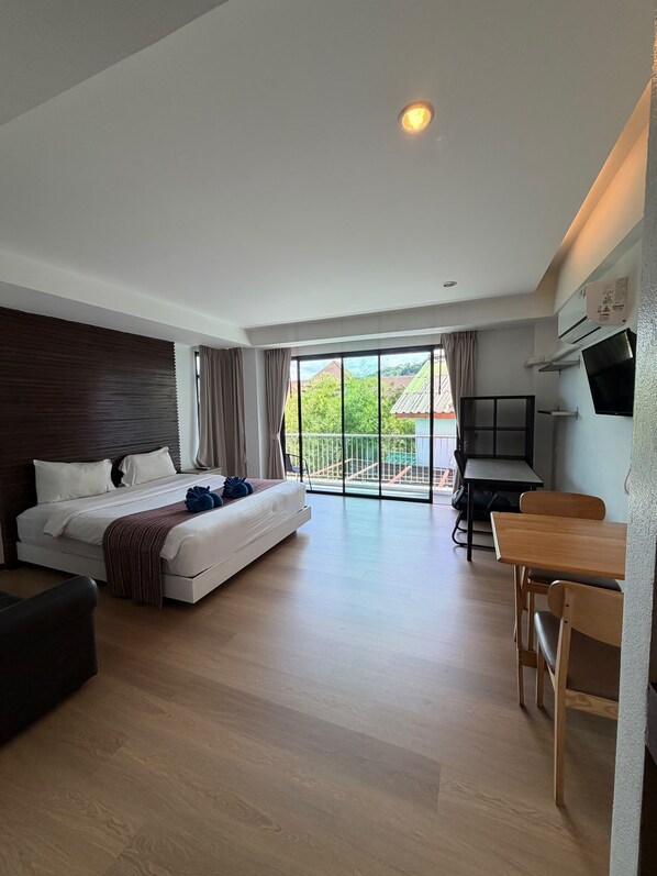 A modern hotel room with a large bed, a desk, and a balcony with a view.