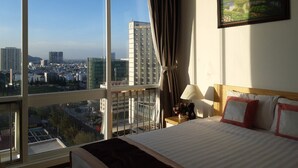 A hotel room with a large window offering a city view, a bed with red and white bedding, and a painting on the wall. - The Grand Condotel (Ho Chi Minh City)