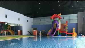 An indoor swimming pool with a blue checkered floor, a colorful play structure, and a modern ceiling design. - The Grand Condotel (Ho Chi Minh City)