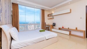 A modern bedroom with a bed, a desk, and a large window offering a city view. - The Grand Condotel (Ho Chi Minh City)
