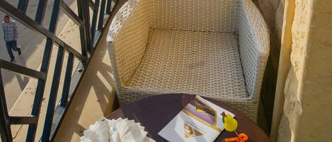 A balcony with a wicker chair, a table with a plate of fruit, a drink, and a brochure. A pyramid is visible in the background.
