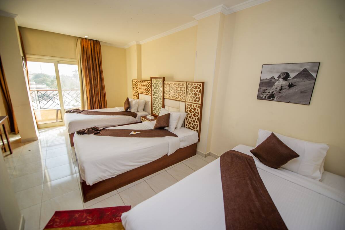 A hotel room with two beds, a balcony, and a wall-mounted photo of the pyramids.