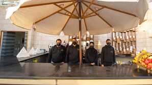 A group of four people standing under a large umbrella in a room with a marble wall and a counter with fruits. - Pyramids Valley (Giza)