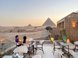 A dining area with tables and chairs overlooking a desert landscape with pyramids in the background.
