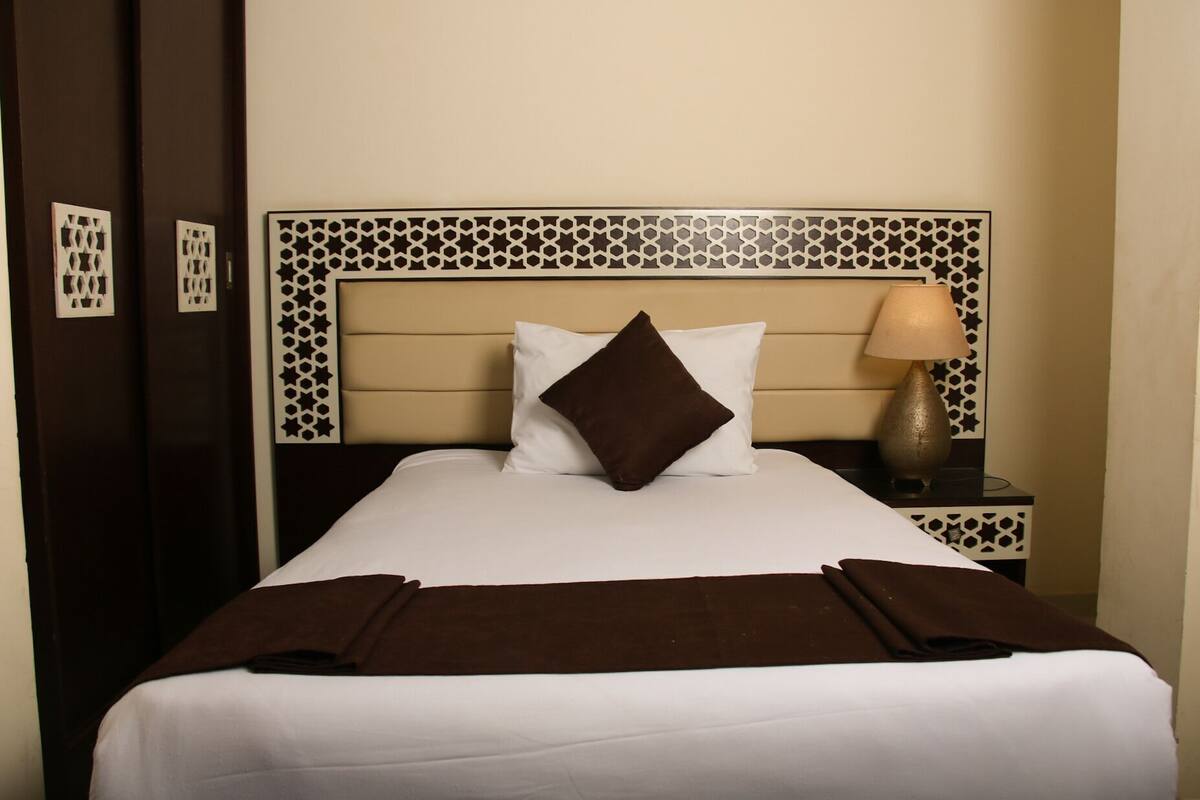 A neatly made bed with a headboard featuring a geometric pattern, a bedside lamp, and a brown throw blanket.