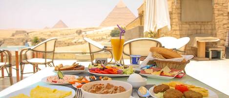 A table set with breakfast items including eggs, bread, and a drink, with a view of pyramids in the background.