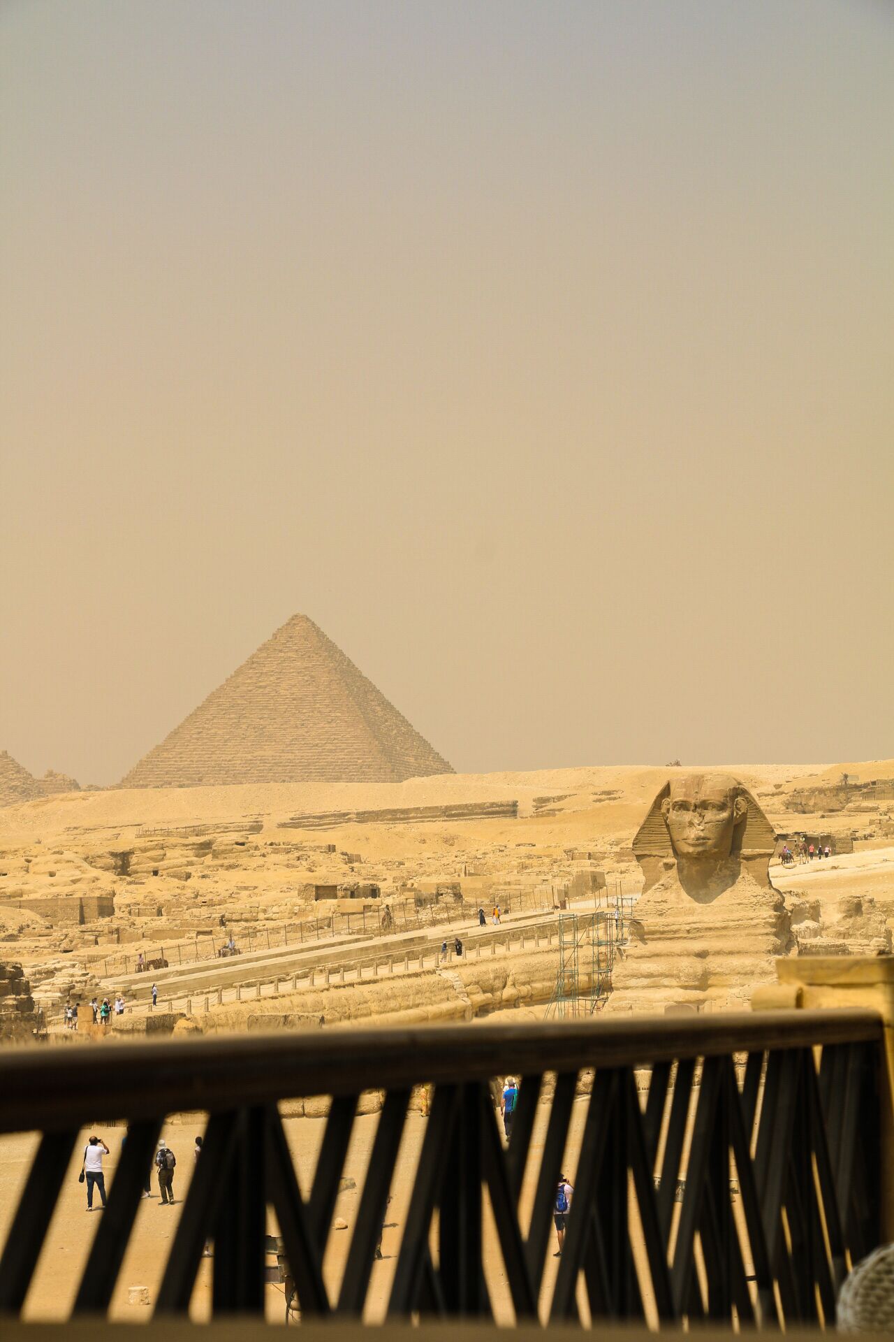 Ett ökenlandskap med pyramider och en stor staty i förgrunden.